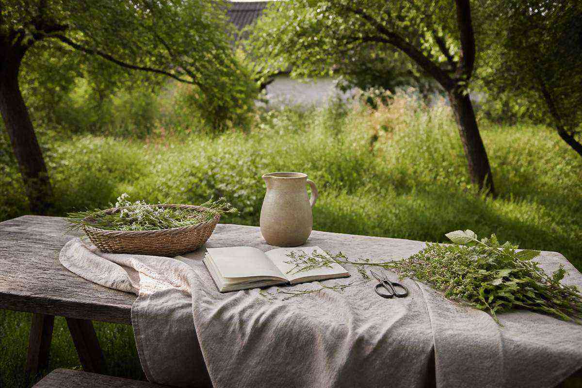 Garden notebook, herbs and linen cloth on a farmhouse table beneath fruit trees