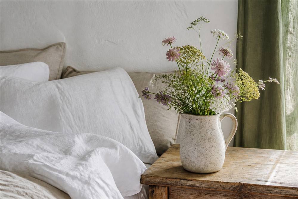 Seasonal garden flowers in a ceramic jug beside natural linen bedding