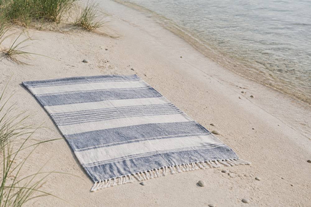 Linen beach towel Blue-grey striped linen towel spread on pale beach sand