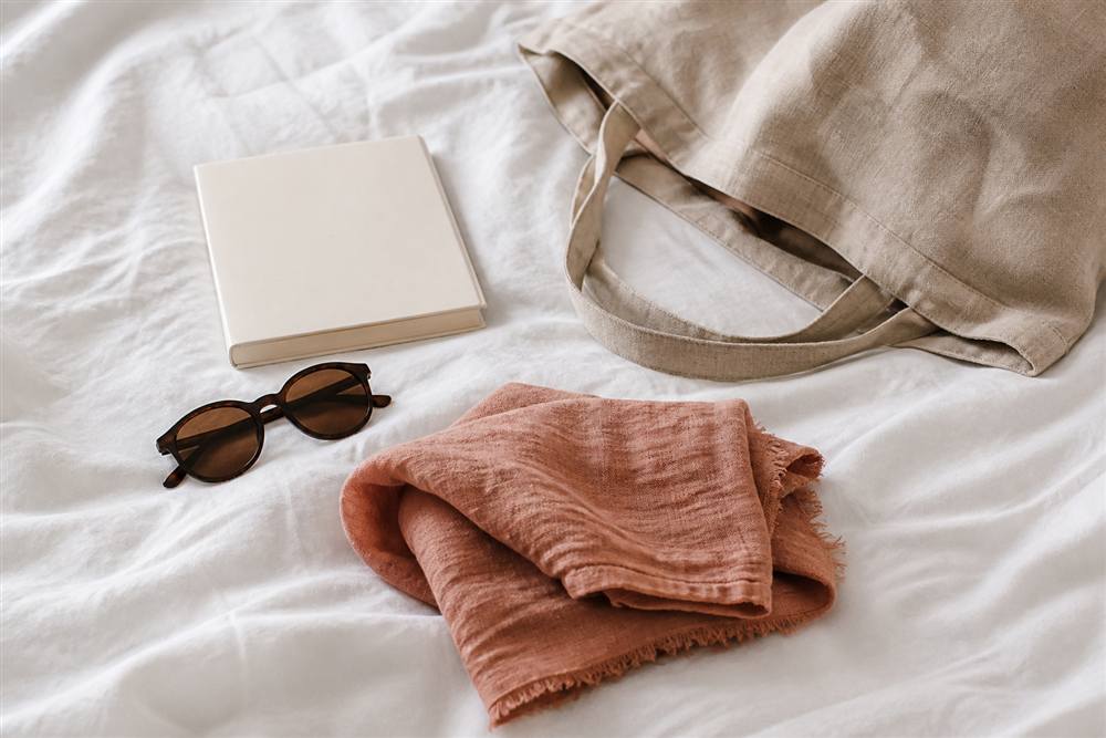Terracotta linen scarf packed with sunglasses, a book and linen tote