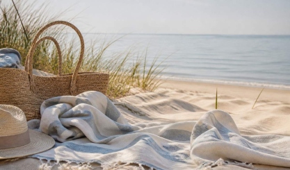 Striped linen beach towel on pale sand beside a woven bag
